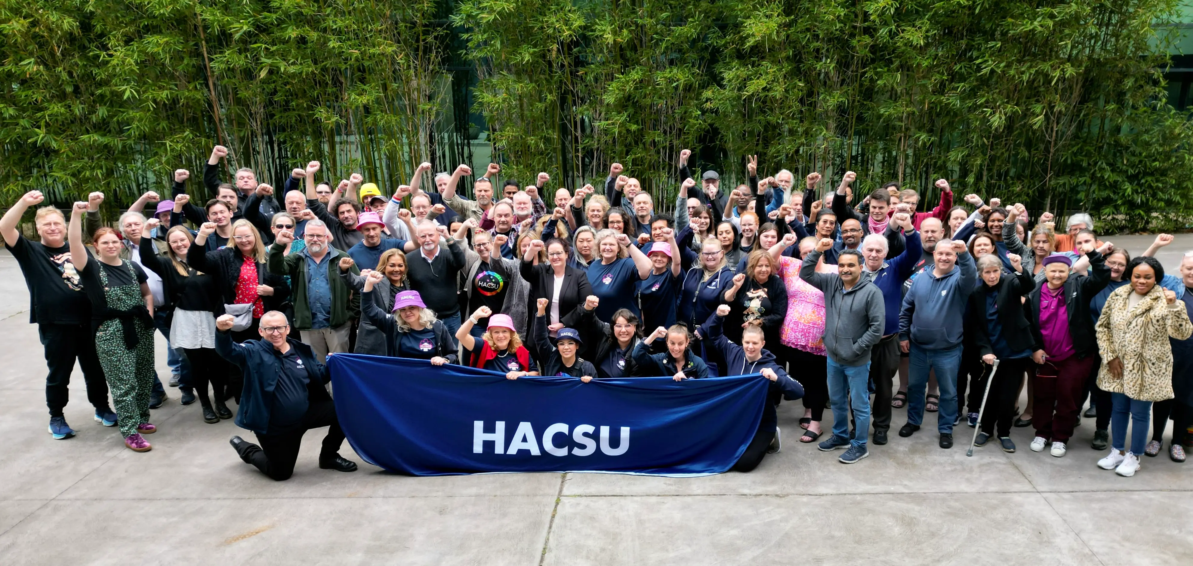 Photo of large group union delegates and activists at the 2023 HACSU annual conference, holding a HACSU banner.