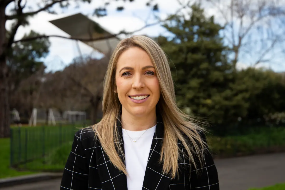 Photo of Elisa Brophy in a blazer, standing in a park.